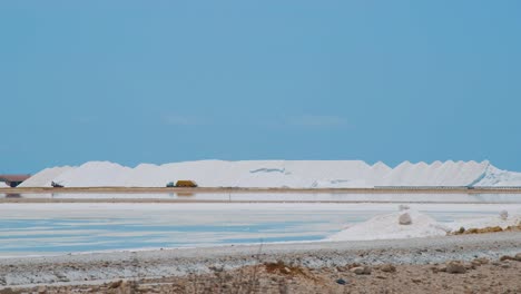 Truck-Loaded-With-Salt-Driving-On-The-Salt-Flat-In-Bonaire,-Netherlands-On-A-Sunny-Day---wide-shot