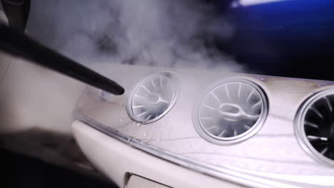 Zooming-FHD-shot-of-a-hot-steam-cleaner-cleaning-the-air-conditioning-vents-in-a-futuristic-car-dashboard,-with-hot-steam-coming-out-of-the-vents