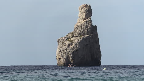 The-finger-of-God-as-two-men-approach-paddlesurfing-in-Cala-Benirras,-Ibiza,-Spain