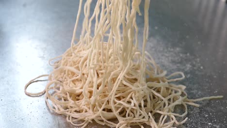 Close-up-Footage-of-Chef-Scattering-Egg-Noodles-on-Shiny-Silver-Table