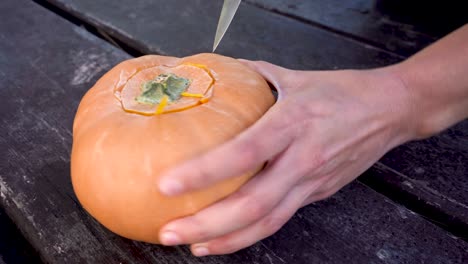 Hands-cutting-off-the-lid-of-a-pumpkin,-preparing-evil-pumpkin-for-Halloween