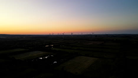 Aerial-shot---side-panning-motion-over-Puck-wind-farm-on-sunset,-rotating-wind-turbines-silhouette-on-orange-sky-background,-Pomorskie,-Poland