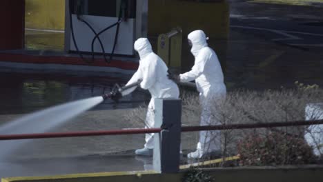 Two-men-in-biohazard-suits-clean-the-floor-of-a-gas-station-with-a-water-stream-coming-from-a-firefighter-hose-during-COVID-19-pandemic