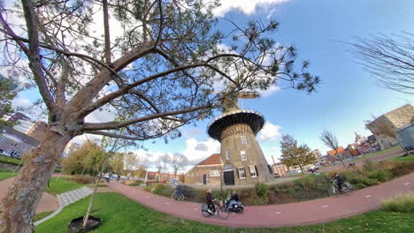 Forward-fish-eye-shot-of-historic-de-valk-windmill,museum-and-riding-cyclist-in-Leiden-City,Netherlands