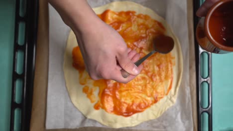 Frau-Verteilt-Tomaten-Auf-Pizzateig-Und-Bildet-Kreise-Mit-Einem-Löffel-Aus-Der-Draufsicht