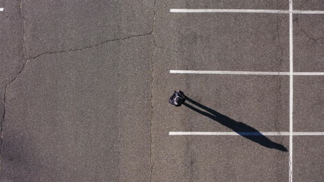 A-top-down-shot-directly-over-an-empty-parking-lot-with-a-man-playing-with-an-electric-remote-controlled-car
