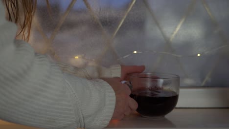 Frau-Mit-Einer-Tasse-Heißem-Kaffeegetränk-Im-Winterfenster,-Mittlere-Aufnahme