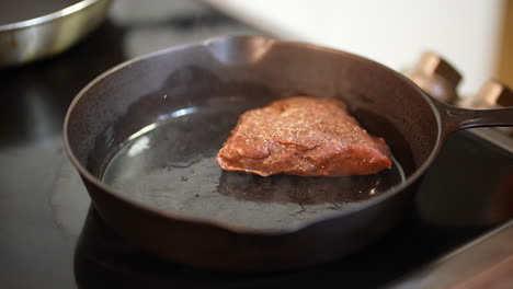 Slow-motion-of-sirloin-steak-going-into-cast-iron-with-oil
