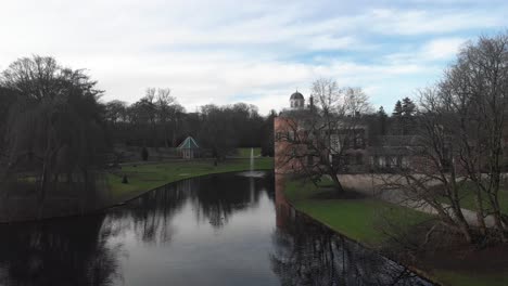 Aerial-approach-of-Rosendael-castle-manor-with-barren-winter-trees-with-the-monumental-building-reflecting-in-the-still-water-of-the-moat-in-the-foreground