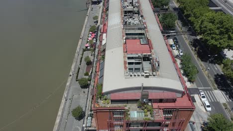 Drone-Flying-Above-Waterfront-Restaurants-Along-Rio-Darsena-Sur-In-Puerto-Madero,-Buenos-Aires,-Argentina---aerial-tilt-up