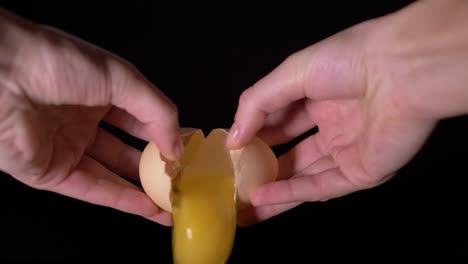 Cracking-egg-and-letting-it-fall-into-a-bowl-filled-with-beaten-eggs-on-a-black-background-in-slow-motion