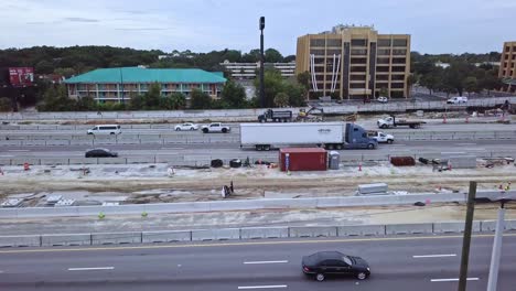 Low-aerial-panning-drone-shot-of-busy-highway-with-road-construction-zone-showing-cars-and-trucks-and-buildings-in-background
