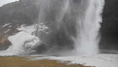 Statische-Zeitlupenaufnahme-Von-Wasser,-Das-An-Einem-Bewölkten-Herbsttag-In-Island-Am-Skogafoss-Wasserfall-Auf-Den-Verschneiten-Boden-Trifft