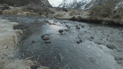 Panning-up-shot-of-a-running-river-surrounded-by-snow-capped-mountains-in-New-Zealand-during-winter