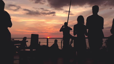 Background-with-silhouettes-of-people-standing-on-balcony-at-restaurant-and-watching-colorful-sunset