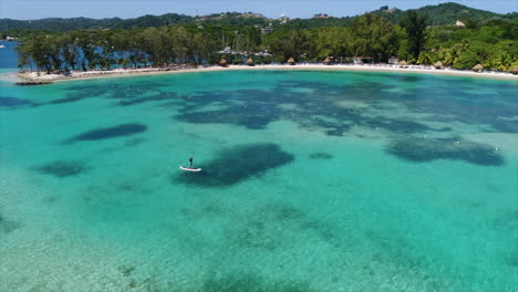 Slow-motion-aereal-view-of-people-paddleboarding-near-a-resort’s-beach-on-the-Honduran-caribbean-sea