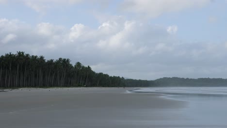 Slow-motion-shot-of-wide-and-long-sandy-beach-with-tall-palm-trees-and-cloudy-sky-in-Asia