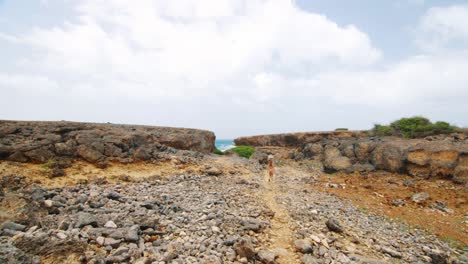 Distant-girl-in-bikini-walks-through-rocky-coast-landscape,-Curacao,-Slow-Motion