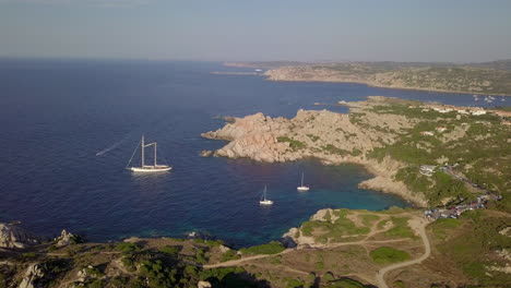 Drone-shot-flying-over-a-wild-rocky-bay-in-north-Sardinia-with-some-sailing-yachts-moored-up-in-it