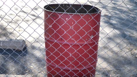 Slow-pan-shot-by-a-grungy-red-garbage-bin-on-the-other-side-of-a-chainlink-fence