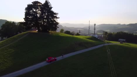 Ein-Roter-Ford-Focus-RS-Fährt-Langsam-Hinter-Einem-Fahrradfahrer-In-Einer-Wunderschönen-Schweizer-Landschaft-Bei-Sonnenuntergang-Her