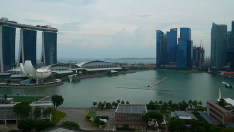 Singapur---Tiro-Panorámico-De-Lapso-De-Tiempo,-Amplia-Panorámica-Con-La-Famosa-Bahía-Marina-De-Singapur-Y-El-Hotel-Sands-Y-La-Silueta-De-Rascacielos-Del-Distrito-Financiero,-Cielo-Nublado-Durante-El-Día