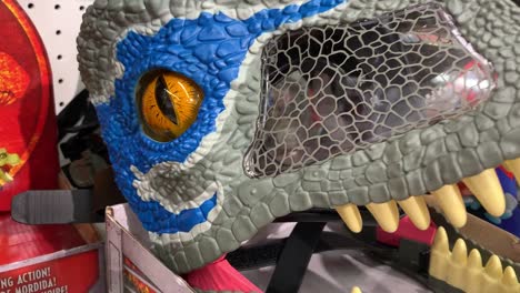 Close-up-of-a-hand-opening-and-closing-the-jaws-of-a-boxed-Velociraptor-Blue-"Chomp-'N-Roar"-toy-mask,-made-by-Mattel-toy-company