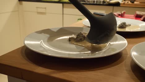 A-white-hand-model-is-preparing-morel-sauce-on-a-white-plate-with-a-black-ladle