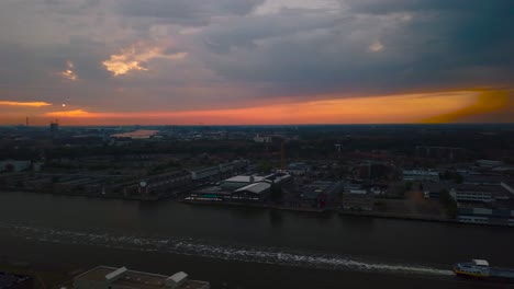 Flying-over-Amsterdam-skyline-by-sunset-by-drone-over-the-IJ-river-near-central-station-with-beautiful-red-sky-and-white-train-heading-to-train-station