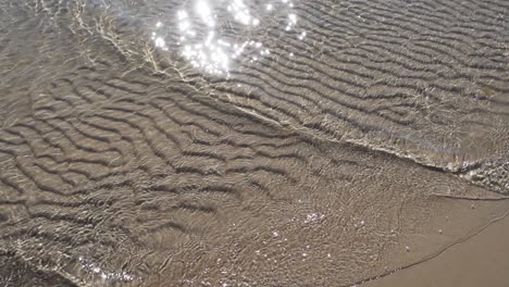 Zeitlupe-Ruhiger-Meereswellen-An-Einem-Sandstrand-Mit-Lichtreflexion-Auf-Dem-Wasser