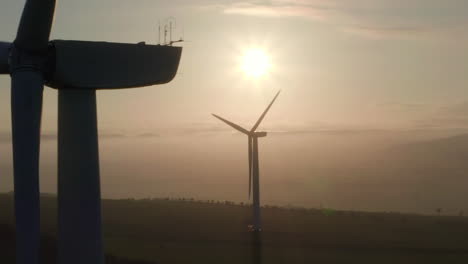 An-aerial-view-of-windfarm-turbines-slowly-turning-with-the-evening-sun-behind-them,-Aberdeensire,-Scotland