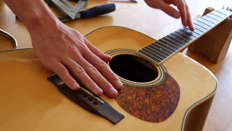 Close-up-hands-of-a-luthier-craftsman-measuring-and-leveling-an-acoustic-guitar-neck-fretboard-on-a-wood-workshop-bench-with-lutherie-tools