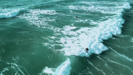 A-drone-shot-of-a-surfer-catching-a-small-wave,-surfing-towards-the-shoreline