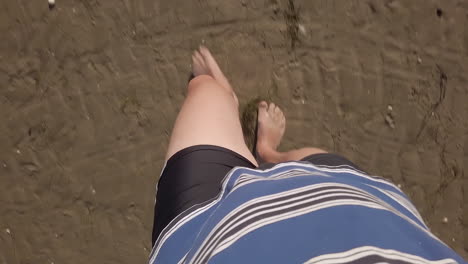 First-person-view-of-a-man-walking-on-wet-sand,-blue-polo-shirt-and-black-shorts