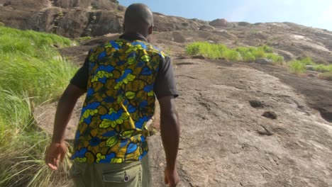 Slow-motion-tracking-shot-from-behind-of-an-African-man-climbing-up-a-steep-granite-hill-in-the-hot-African-sun