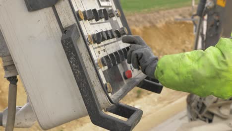 A-construction-worker-in-work-clothes-holds-a-hand-on-the-knobs-of-control-panel-and-controls-the-machine