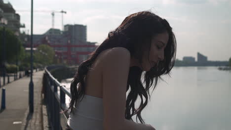 Beautiful-latina-woman-on-holiday-leaning-against-the-railing,-looking-at-the-river-Thames-in-London,-thinking,-smiling-and-wandering