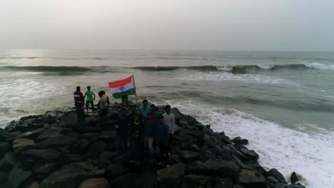 Group-of-Patriotic-youthful-men-hold-Indian-national-flag-standing-on-a-rocky-beach-front-with-waves-crashing