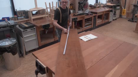 Woodworker-measuring-dimensions-of-lumber-on-workbench-with-measuring-tape