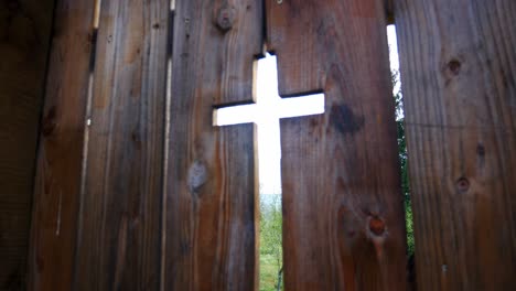 Old-wooden-gate-with-a-cross-shaped-hole-that-gives-entrance-to-a-cemetery-and-church