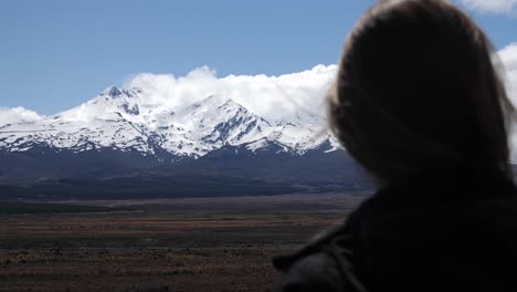 A-snow-capped-Mount-Ruapehu-looms-in-the-distance-as-a-female-tourist-looks-at-the-mountain
