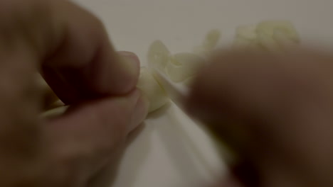 Close-Up-Hand-Cutting-Garlic-With-Small-Kitchen-Knife-On-Cutting-Board