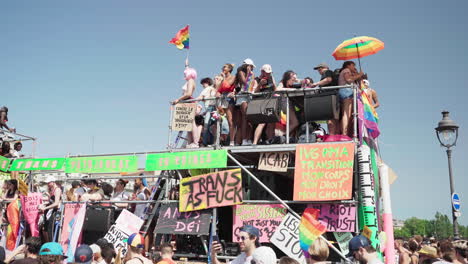 Close-up-of-people-partying-on-top-and-inside-of-a-vehicle-colorfully-decorated-that-is-passing-through-the-people-at-the-Gay-Pride-march-in-Paris,-France