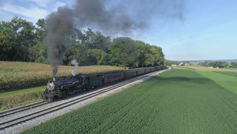 Aerial-View-on-a-Steam-Passenger-Train-Leaving-a-Train-Station-in-the-Amish-Countryside-on-a-Summer-Day