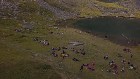 Aerial-circle-around-a-large-group-of-people-who-relax-at-a-mountain-lake,-Rodnei-Mountains,-Romania