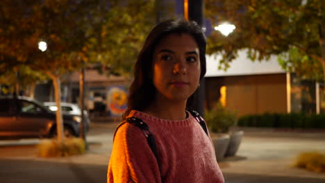 A-beautiful-young-hispanic-woman-walking-and-shopping-at-stores-on-an-urban-city-road-under-street-lights-at-night