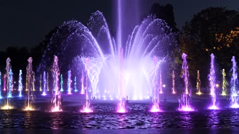 Fountain-illuminated-at-night-in-city-park,-abstract-lights-with-changing-colors-from-multiply-nozzles-in-circle