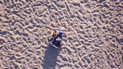 Luftaufnahme-Eines-Jungen-Paares,-Das-Am-Sandstrand-Sitzt-Und-Sich-Umarmt