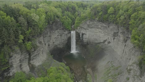Drone-shot,-flying-to-the-right,-showing-a-big-waterfall,-in-a-canyon-with-trees-surrounding-it