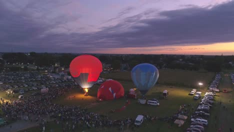 Luftaufnahme-Eines-Heißluftballonfestivals-Bei-Nacht,-Bei-Dem-Propan-Abgefeuert-Wird-Und-In-Einer-Sommernacht-Ein-Nächtliches-Leuchten-Erzeugt